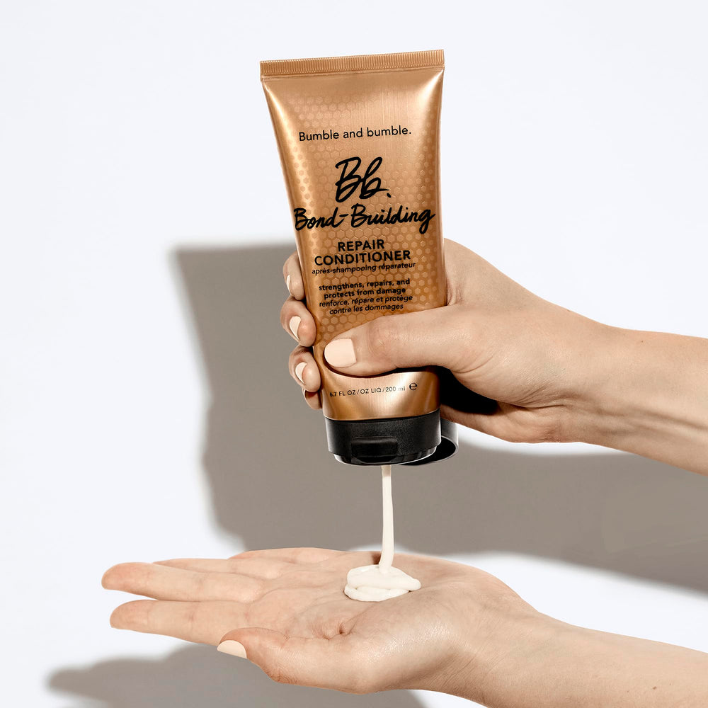 Hands applying Bumble and bumble conditioner to damp hair.