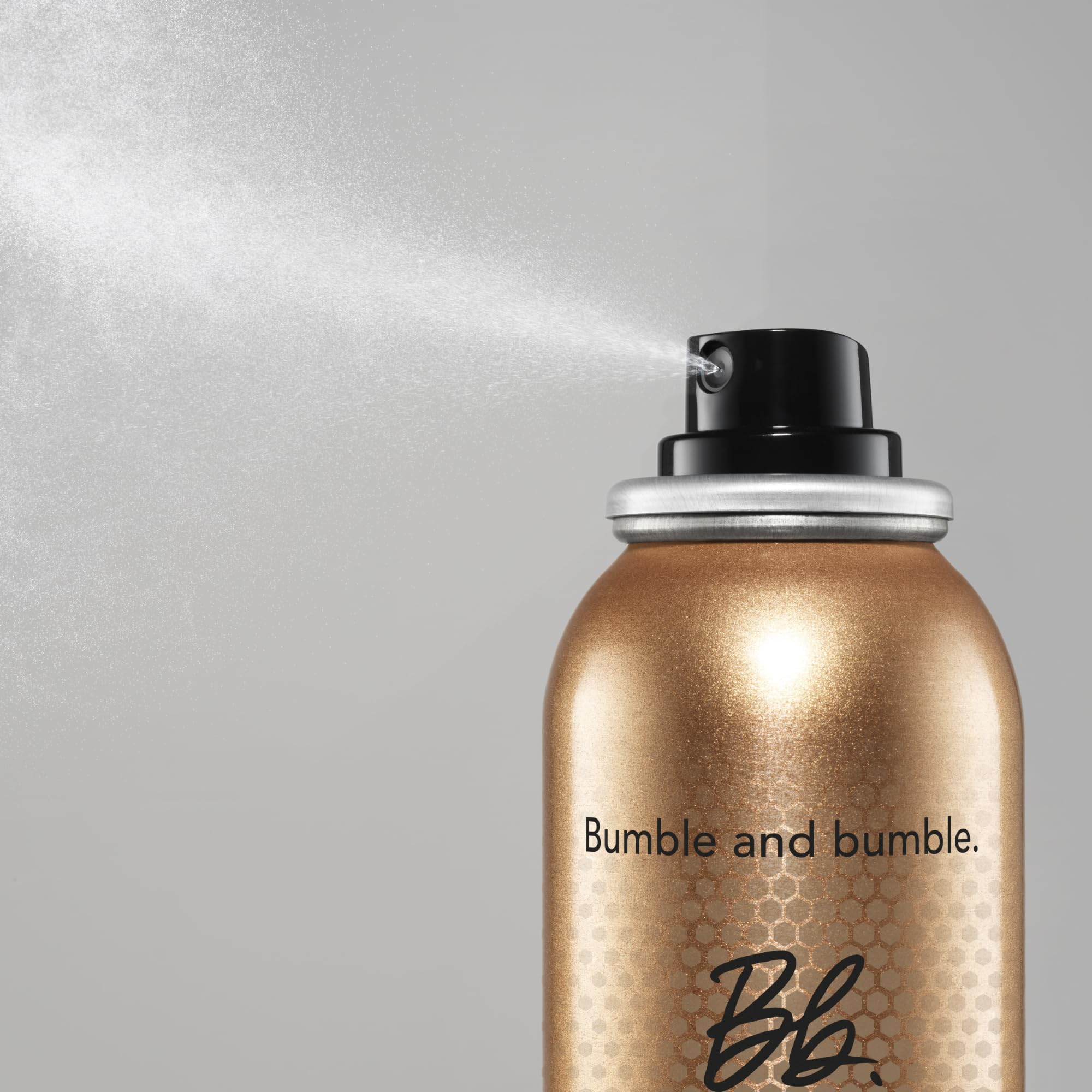Bumble and bumble Heat Shield mist in hand applying to damp hair, reducing frizz and heat damage.
