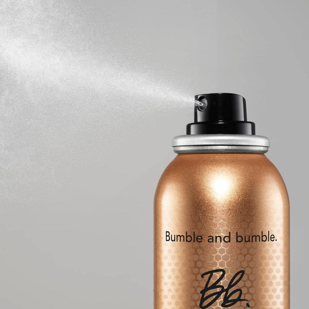 Bumble and bumble Heat Shield mist in hand applying to damp hair, reducing frizz and heat damage.