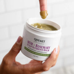 Close-up of Qhemet Biologics balm texture on finger, rich botanicals for scalp nourishment