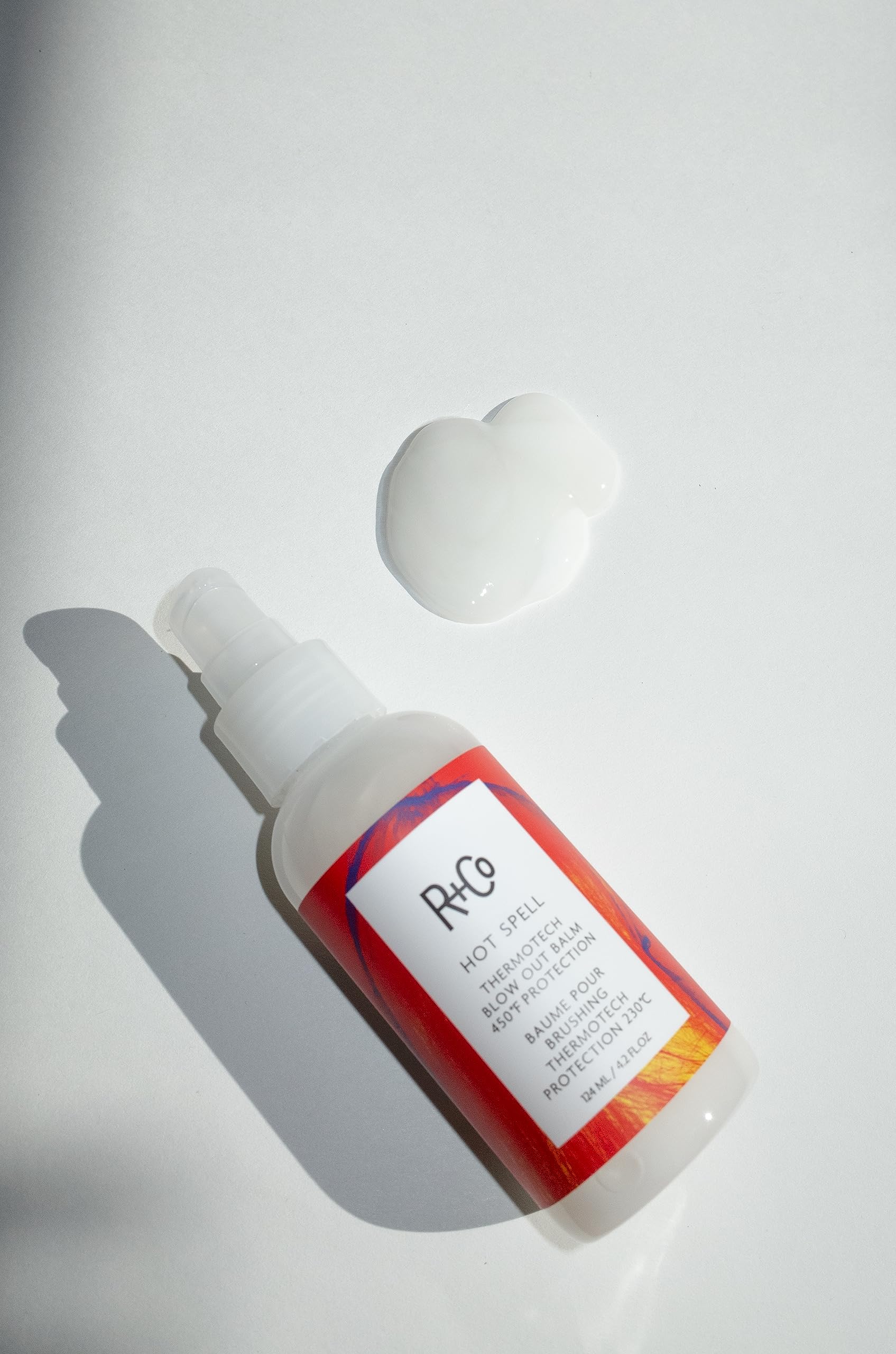R+Co Hot Spell balm being spread into smoothing cream for frizz control